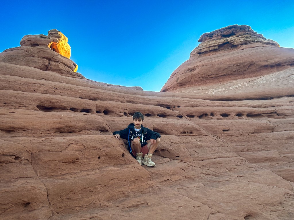 Bastion sitting on red sandstone, looking toward Delicate Arch in the distance at Arches National Park.